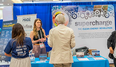 People talk in front of a conference exhibit that says 'supercharge the clean energy revolution'